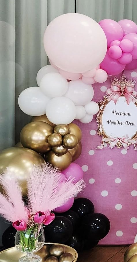 Balloon decor in pastel pink, hot pink, white, chrome gold and black around a pink polka-dot panel with a birthday sign and pink pampas grass